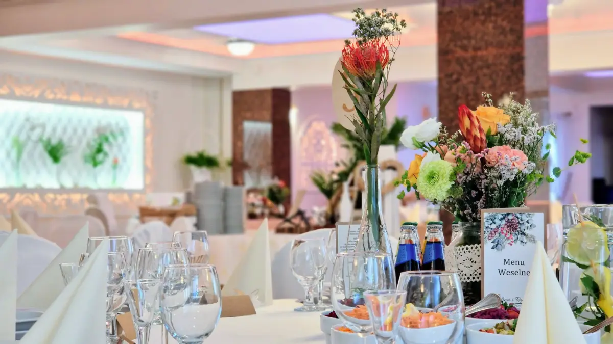 Nakryty stół weselny z menu i bukietem kwiatów, w tle podświetlana ścianka sali